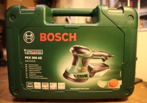 Aufgenommen wurde das Bild auf einer Werkbank. Dort steht der Koffer des Bosch PEX 300 AE Exzenterschleifer.